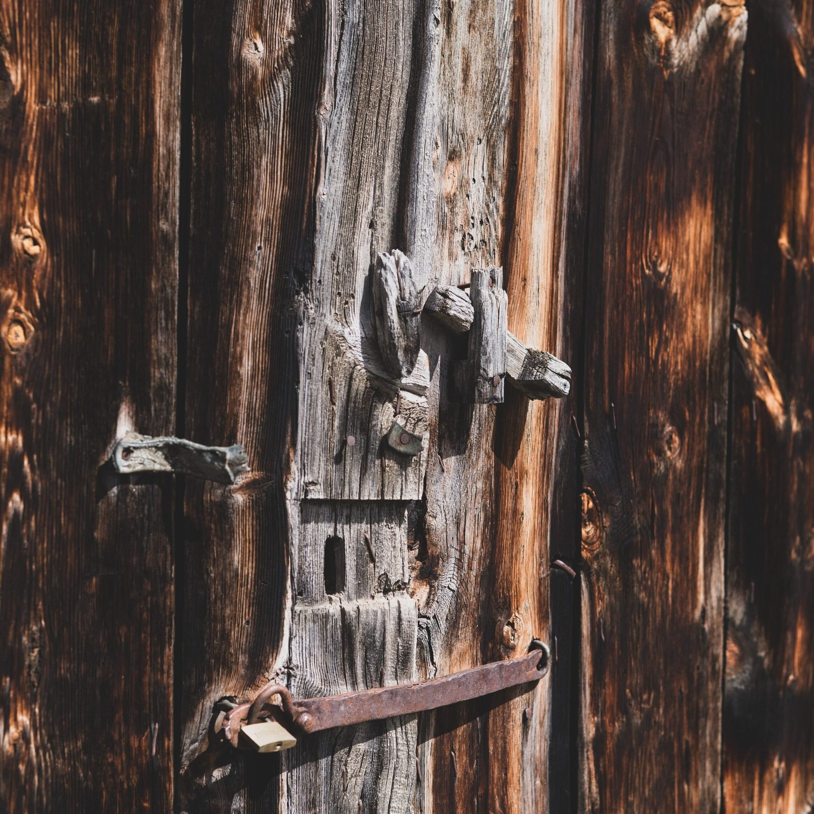 Close-up of a weathered wooden door featuring a vintage lock in a rustic setting.