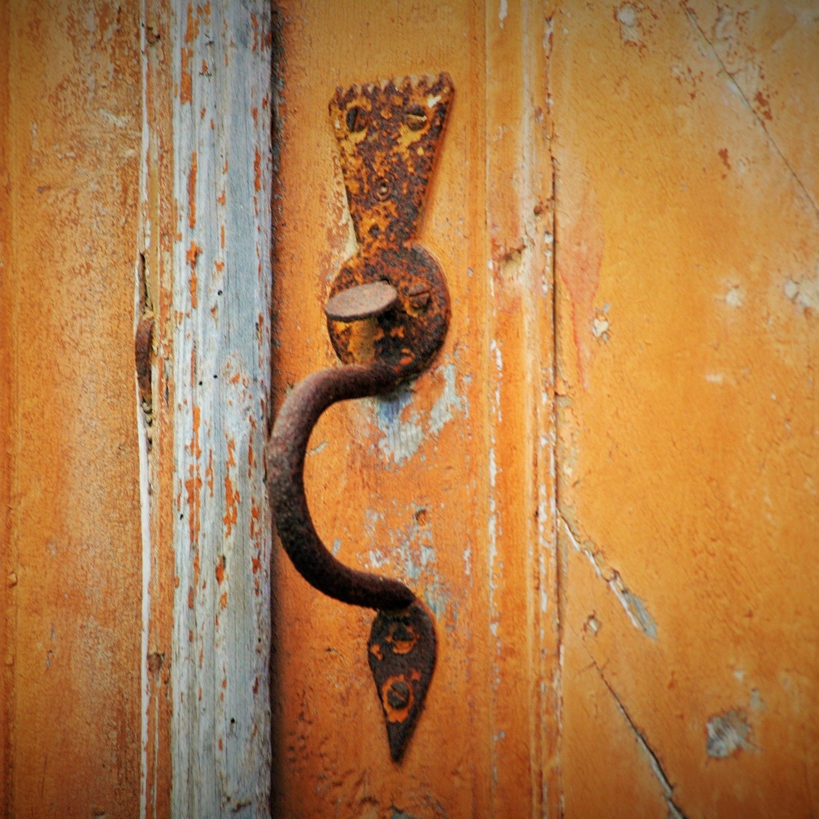 Close-up of a vintage rusty door handle on a weathered wooden door, showcasing rustic charm.